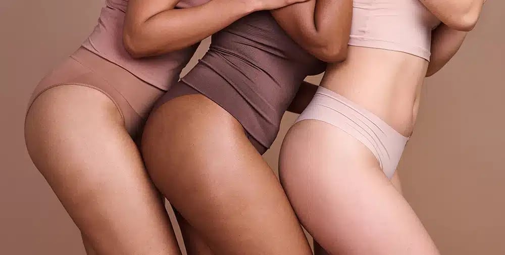 Three women in various shades of underwear standing close together.