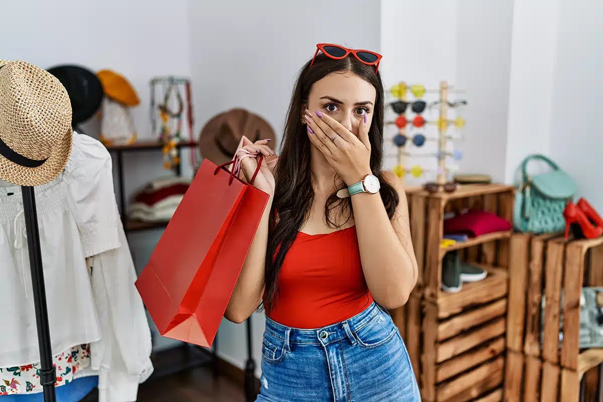 Young brunette woman holding shopping bags at retail shop shocked covering mouth with hands for mistake Young brunette woman holding shopping bags at retail shop shocked covering mouth with hands for mistake
